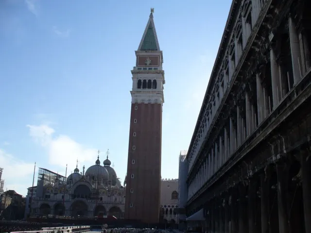 A tall brick bell tower with a green spire beside a basilica