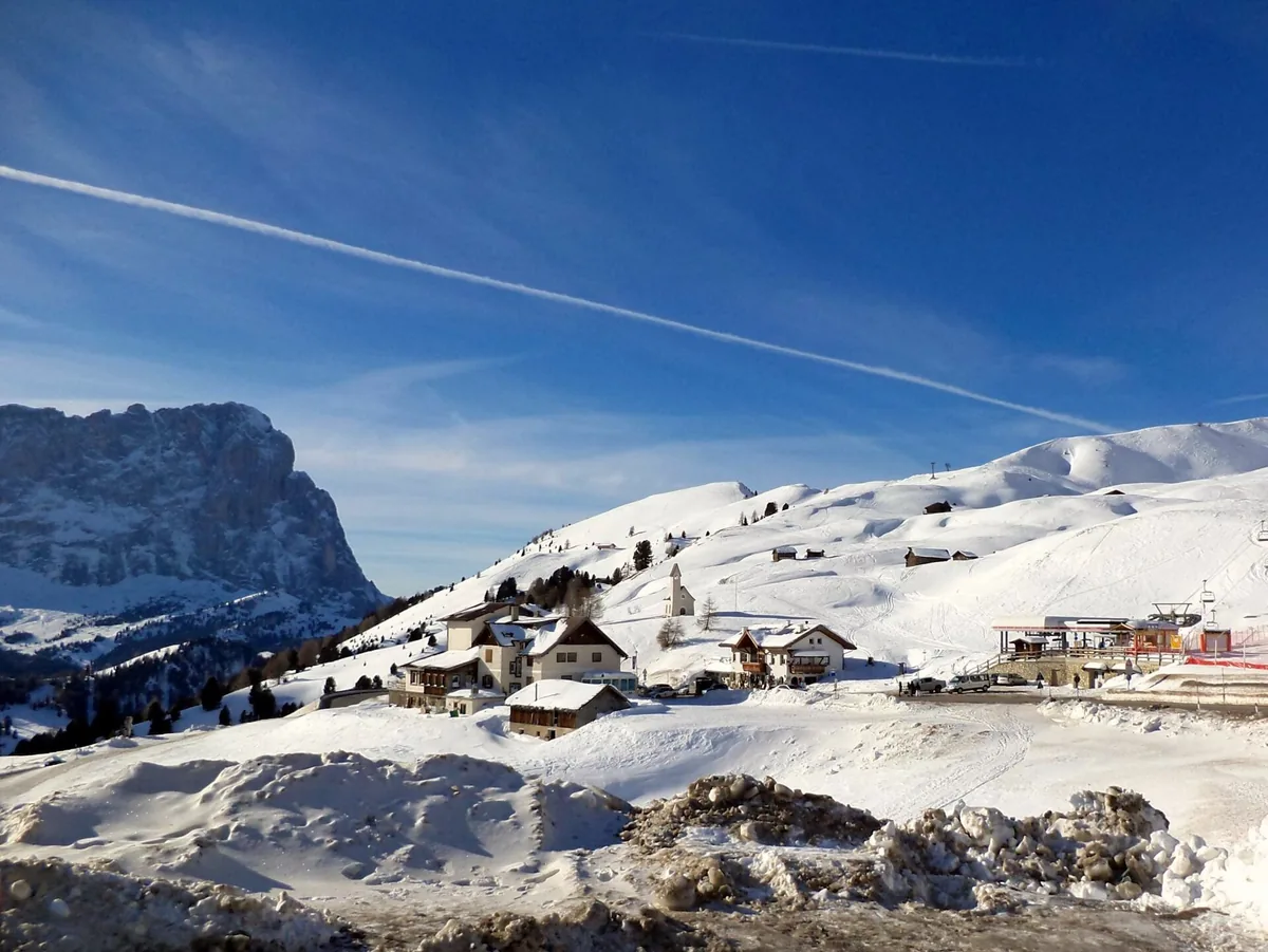 Snowy slopes with alpine wooden houses and a rock wall under a deep blue sky