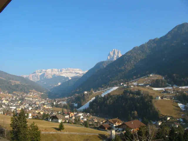 An alpine town on a green valley floor between forested slopes and peaks