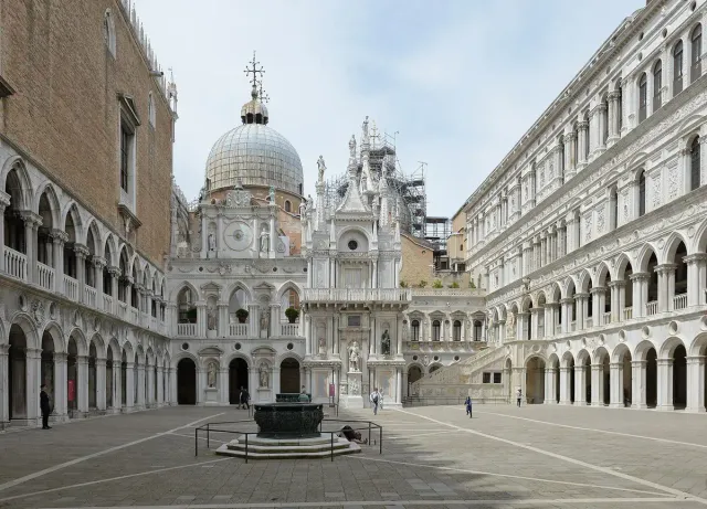 Lead domes and an ornate facade seen across an arcaded stone courtyard