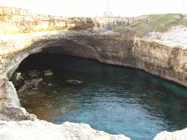 A round sea pool sunk in rock with turquoise water and an opening to the sea