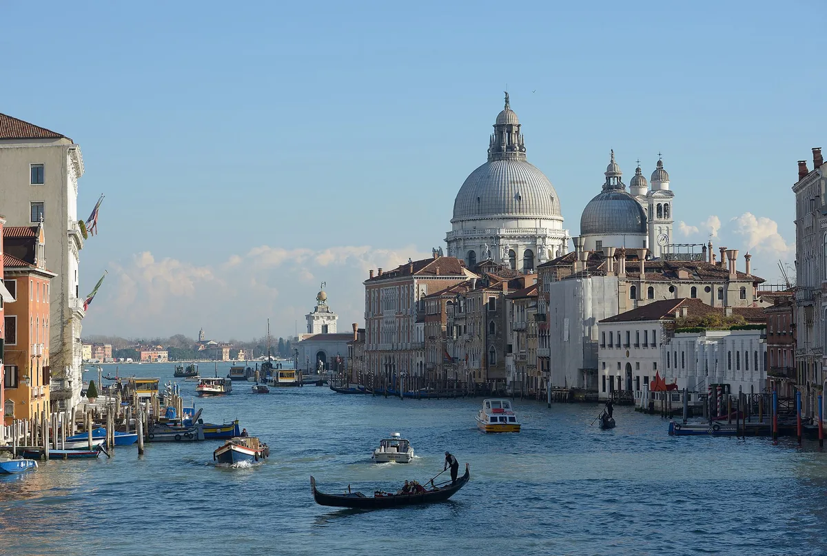 A wide canal with a gondola and boats, and a grey domed church at its end