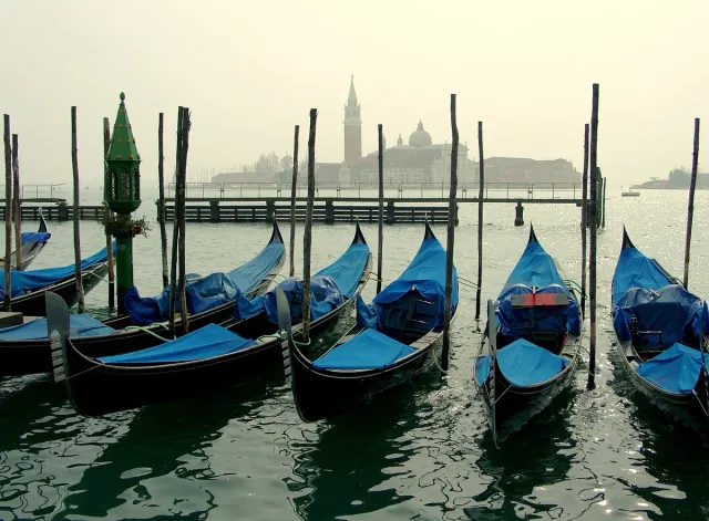 Moored gondolas on the water facing an island church and brick tower