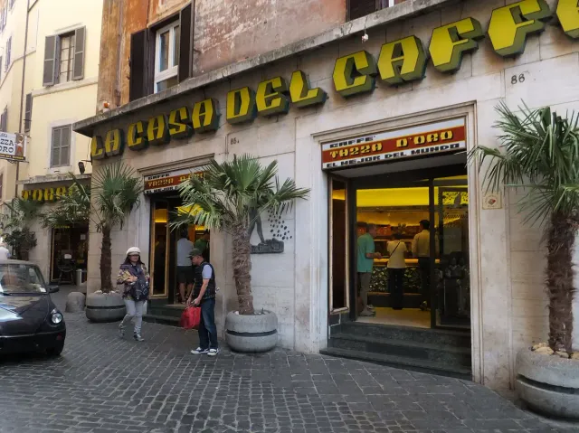 A cafe front with a large gilded sign and customers at the door