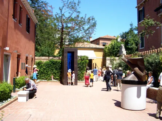 A sculpture garden with visitors between terracotta walls and trees