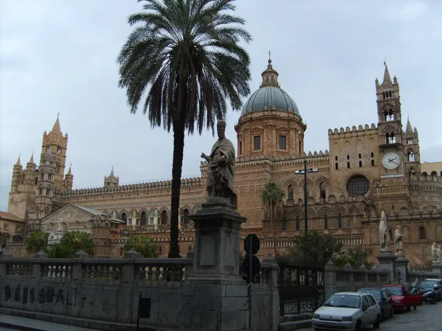 A sandstone cathedral with a dome, towers and a palm in front