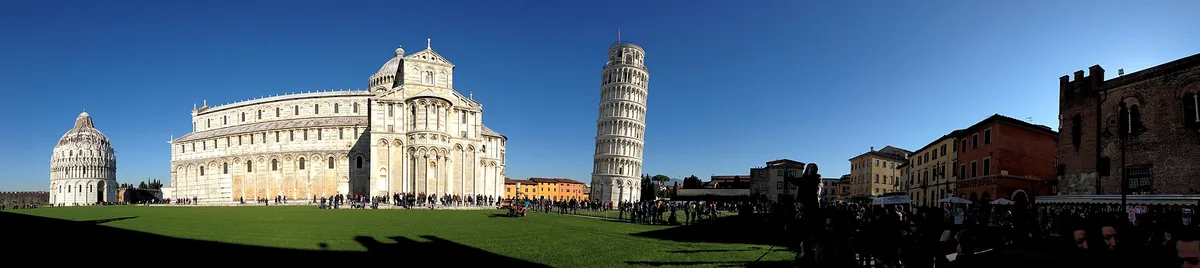 Round leaning white marble bell tower on a lawn beside an arcaded cathedral facade