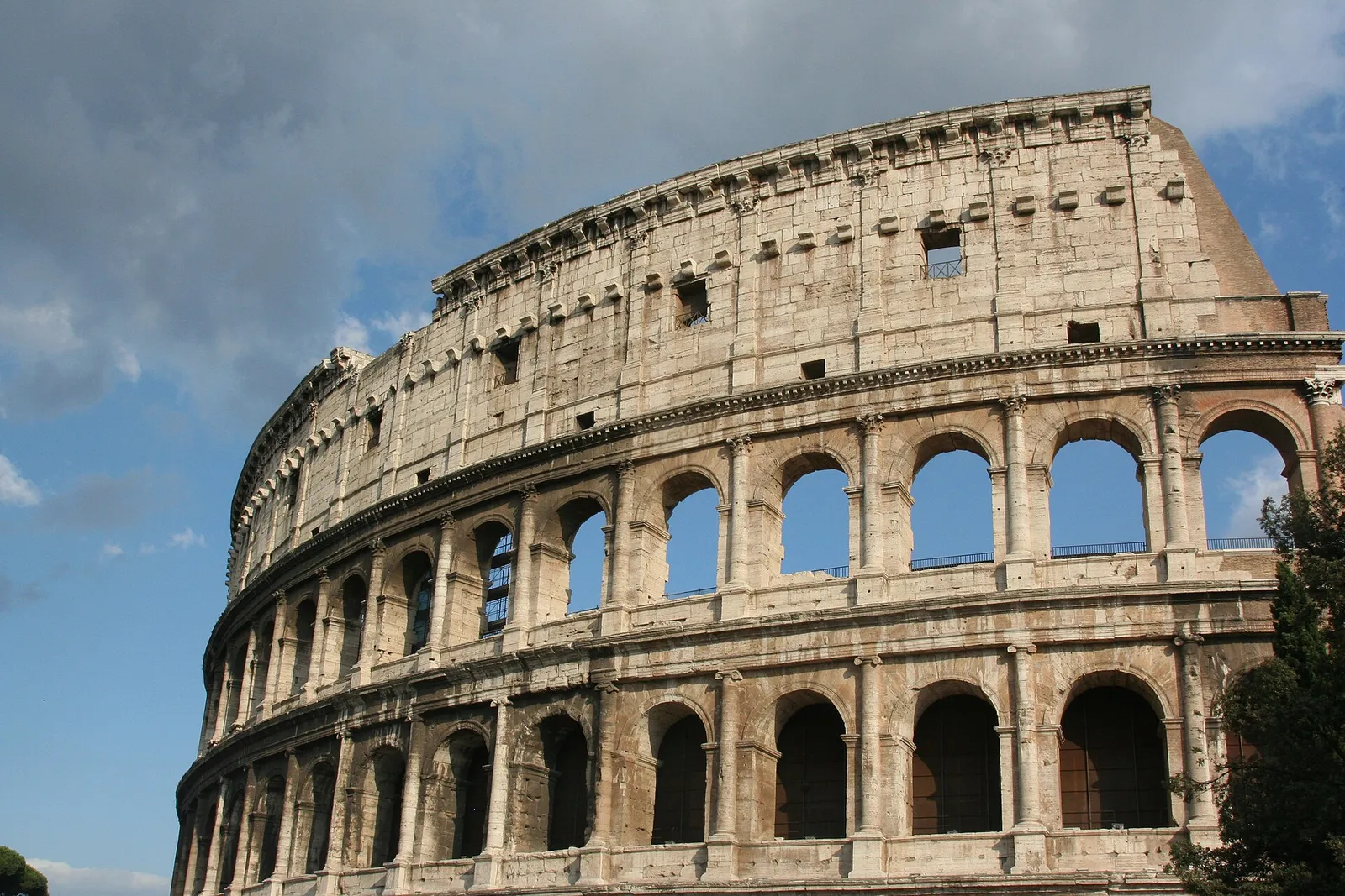 The stone arches of the Colosseum against a blue sky with scattered clouds in Rome, Italy