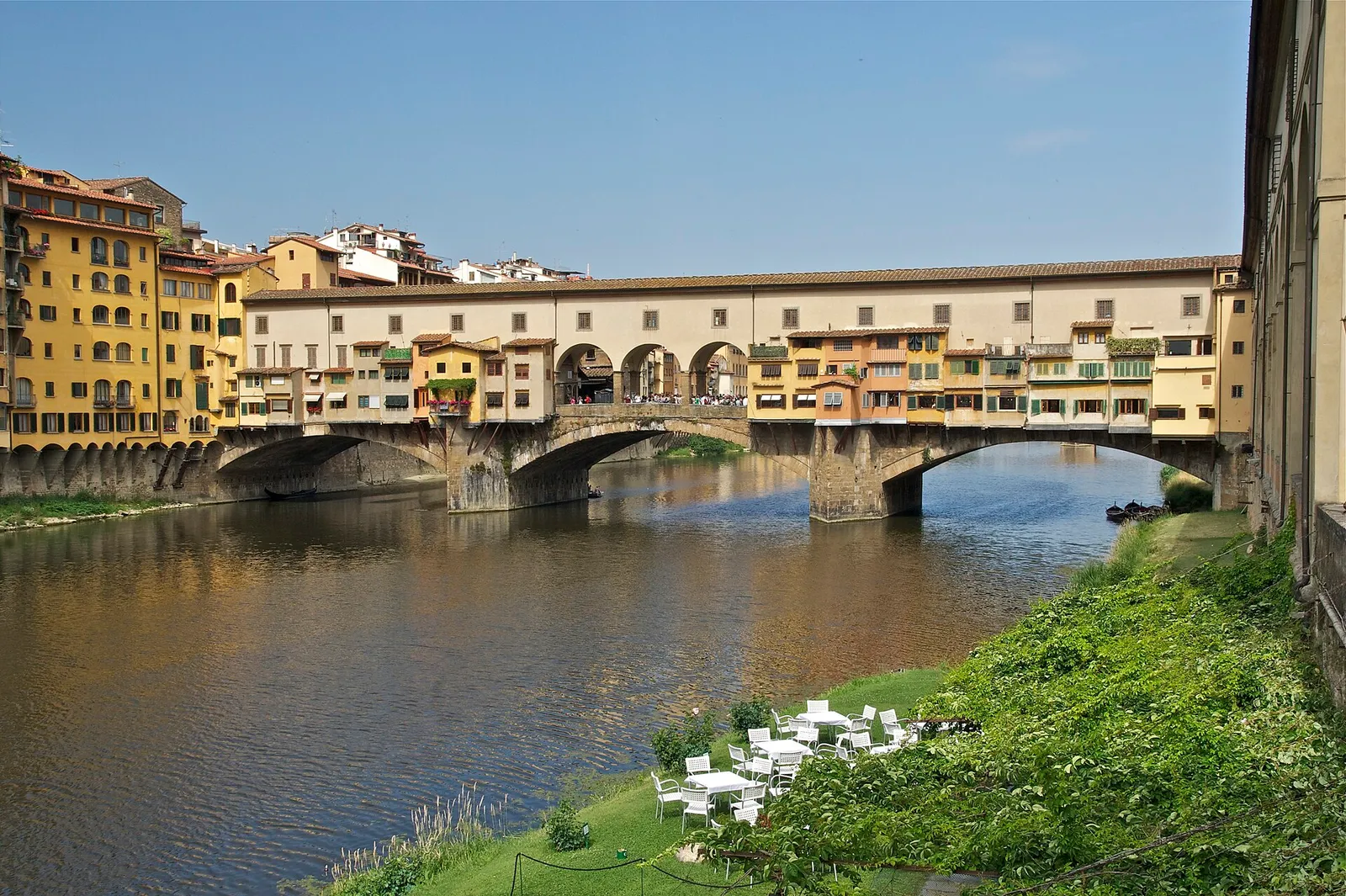 The Ponte Vecchio bridge lined with shops reflected in the Arno river on a clear day in Florence, Italy