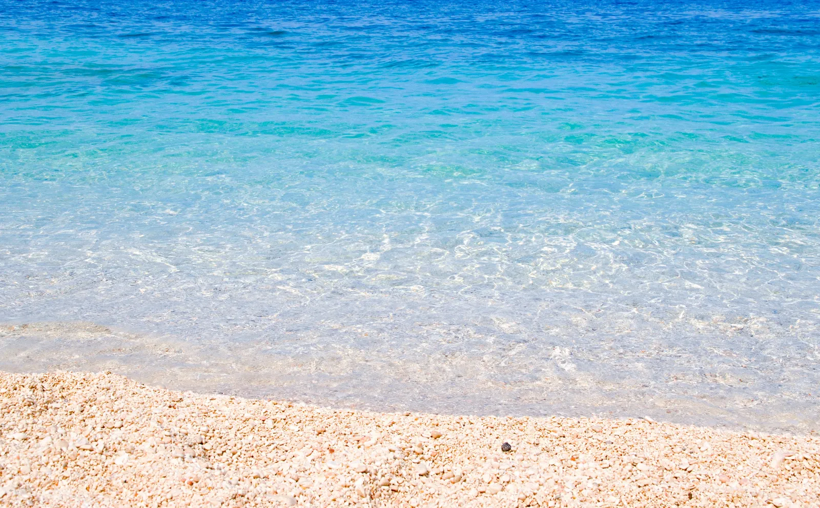 Turquoise water over white sand on the Sardinian coast beside a rocky headland, Italy